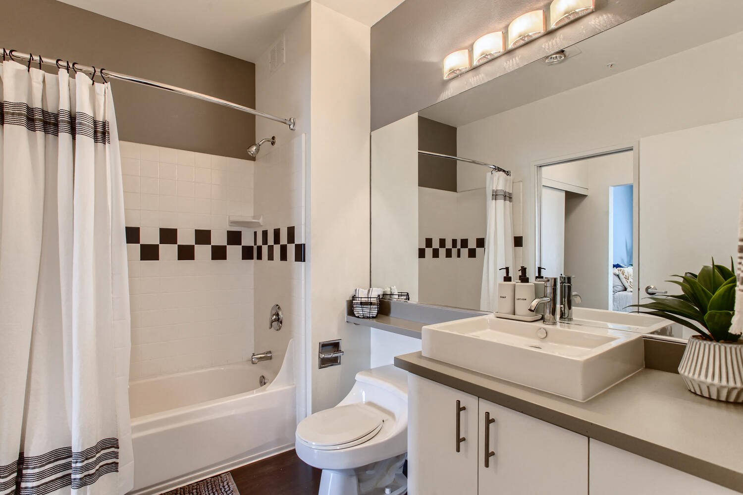 One Bedroom Apartments in Downtown Portland - Linc245 - Bathroom with WoodStyle Flooring, Shower and Tub Combo, Large Vanity Mirror, Sink, and White Cabinets